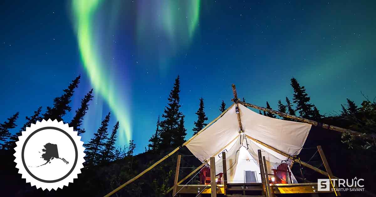 A tent in the wood, under a starry sky and the northern lights in Alaska.