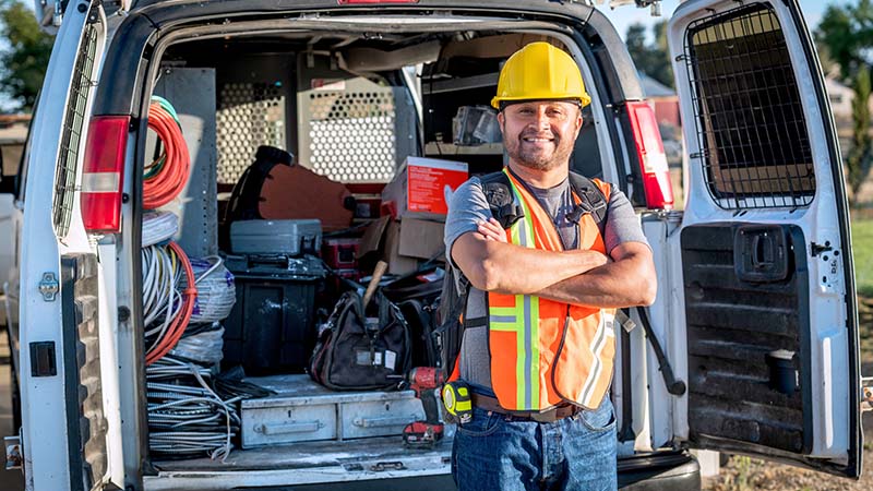 Smiling construction worker standing next to work van.