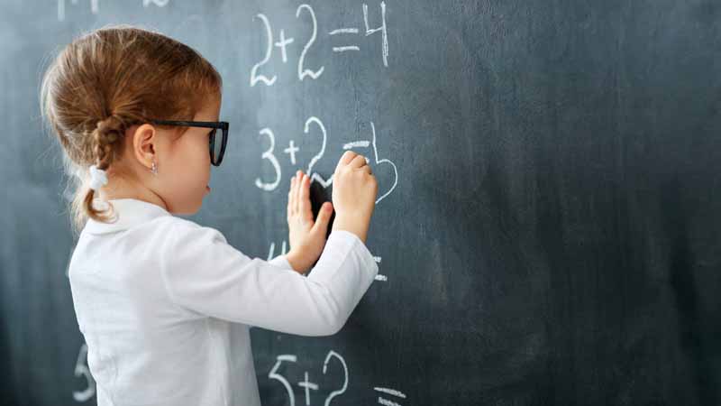 A child writing addition equations on a chalkboard.