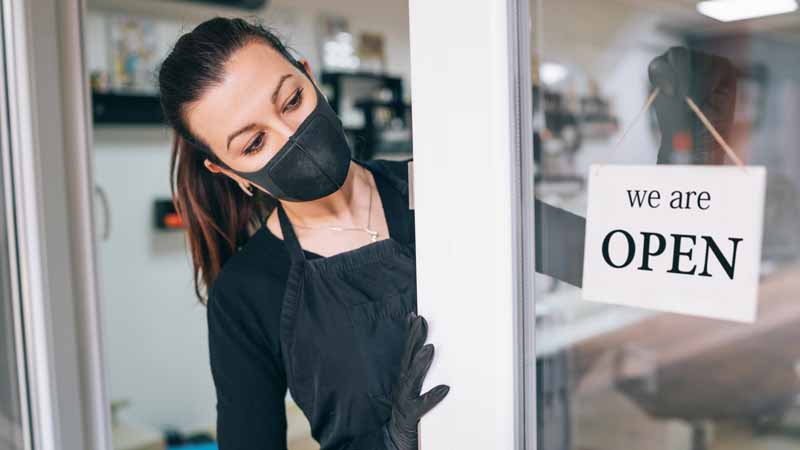 Business owner wearing a mask putting an 'Open' sign in her shop window.