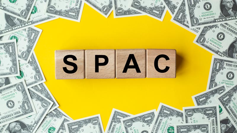 Wooden blocks spelling 'SPAC' surrounded by money.