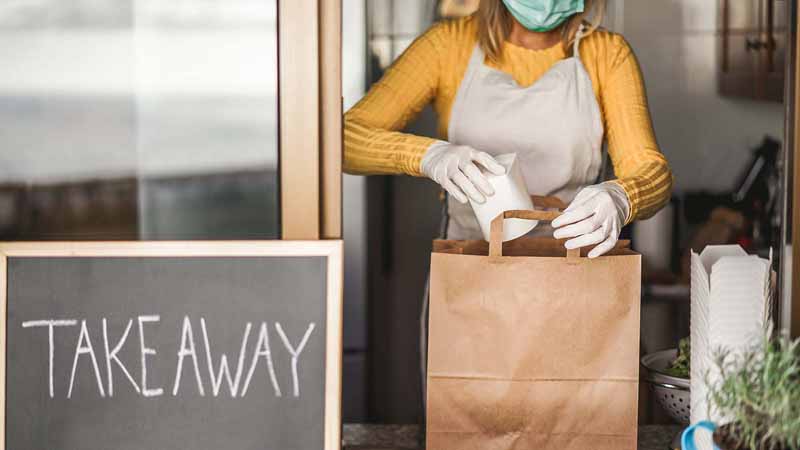 Masked restaurant worker packing a delivery order.