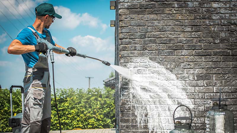Man pressure washing a brick wall.