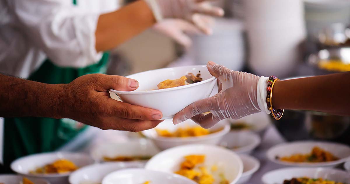 A gloved hand provides a bowl of food to another individual.