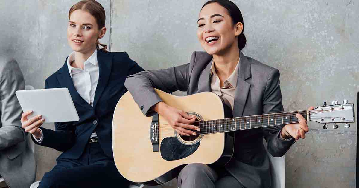 Two women in business suits laughing and playing the guitar.