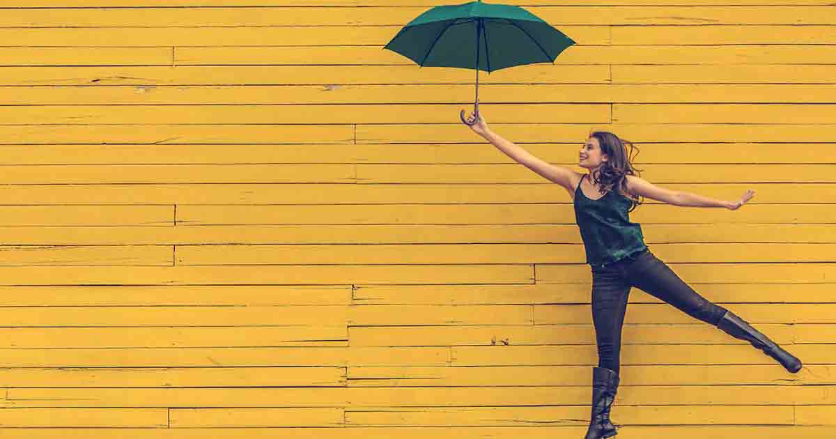 https://startupsavant.comSmiling woman holding umbrella in front of yellow wall